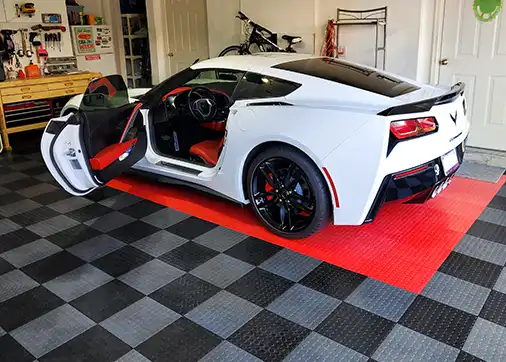 A white Corvette parked in a garage with GarageDeck floor. The tiles are a black and graphite checkerboard with a bright red parking area.