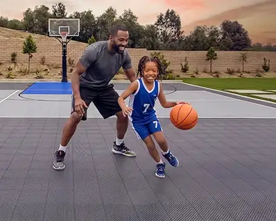 A father plays basketball at sunset with his daughter on their Dunkstar basketball court.